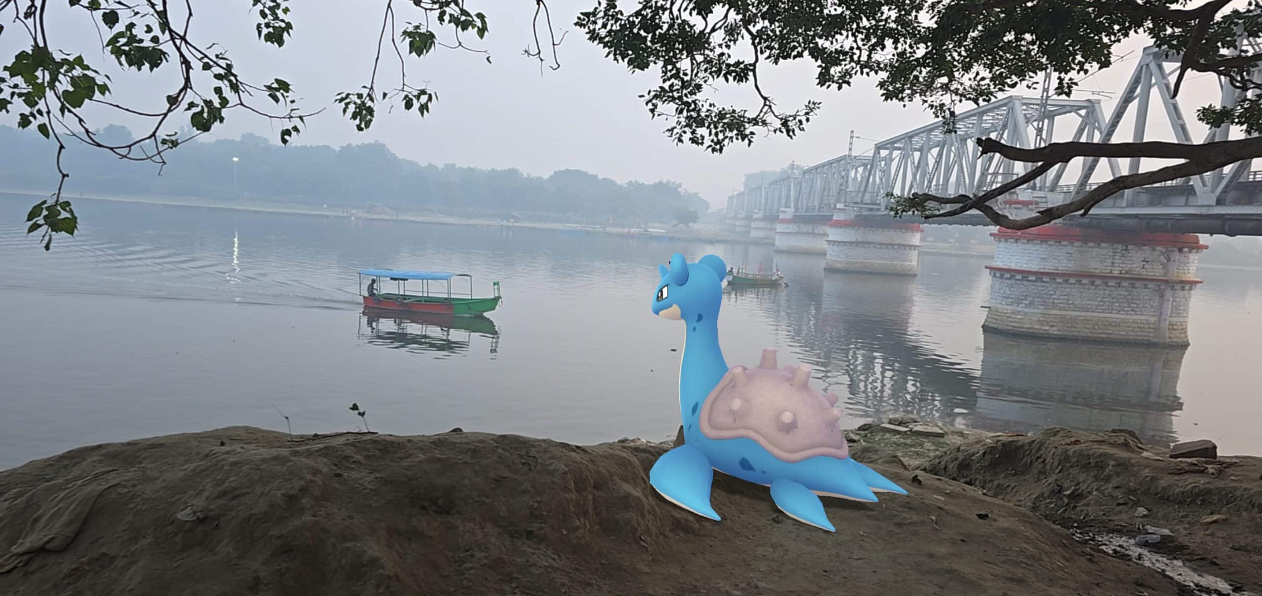 A Lapras sits on a muddy river bank, watching a small boat float by. There is a hazy fog, and a bridge