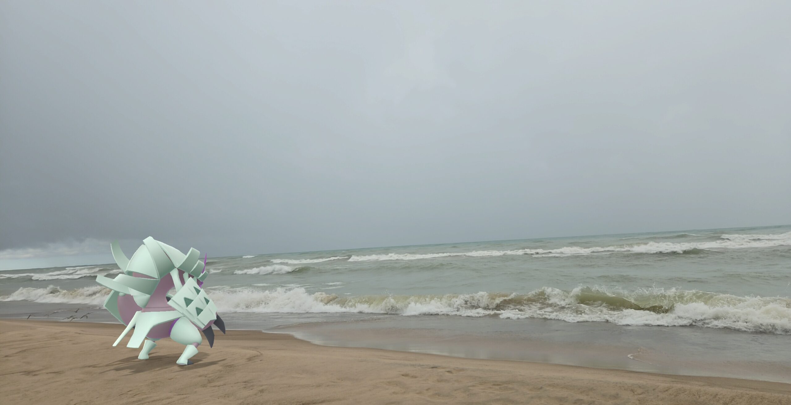As waves crash onto a beach under a dreary, dark looking sky, a Golisopod looks out to sea