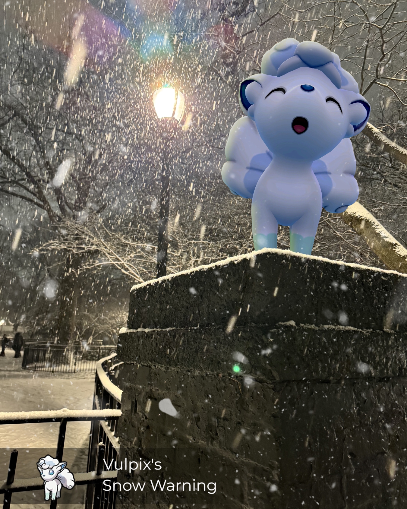An Alolan Vulpix stands atop a brick pillar in the snow at night