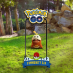 a Fuecoco is shown on a phone screen in the centre of the image, with the Pokémon GO logo above the phone, and the Community Day logo underneath. The setting is a grassy park, with trees in the background, and a rocky wall