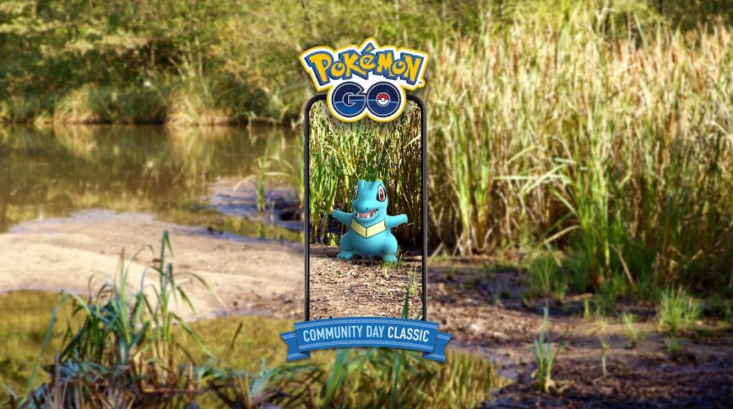 A Totodile is seen among reeds on a pond edge. It is shown as if through a phone screen, with the banner above it saying Pokémon GO, and Pokémon GO Community Day Classic underneath it