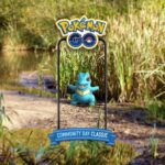 A Totodile is seen among reeds on a pond edge. It is shown as if through a phone screen, with the banner above it saying Pokémon GO, and Pokémon GO Community Day Classic underneath it