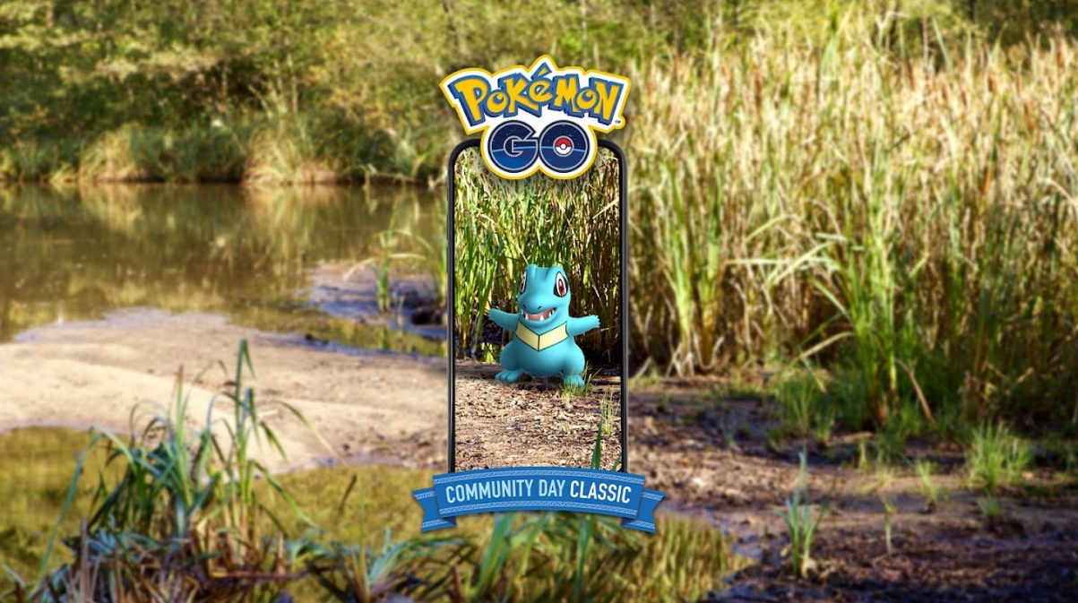 A Totodile is seen among reeds on a pond edge. It is shown as if through a phone screen, with the banner above it saying Pokémon GO, and Pokémon GO Community Day Classic underneath it